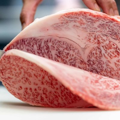 和食レストランの板前が厨房で最高級和牛の霜降り塊肉を丁寧に切り分ける職人技の調理シーン